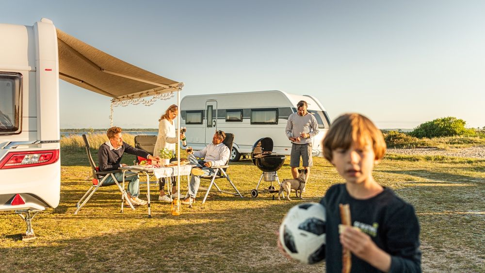 Familie beim Camping mit Wohnwagen, Kind spielt Fußball im Vordergrund