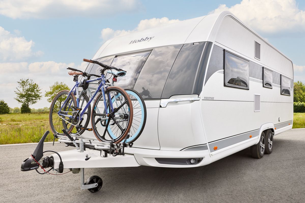 Weißer Hobby-Wohnwagen mit montiertem Fahrradträger und blauem Fahrrad auf Rasenplatz