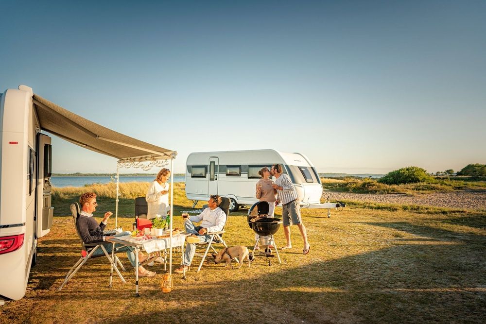 Familie beim Camping mit Wohnwagen kocht und isst gemeinsam im Freien