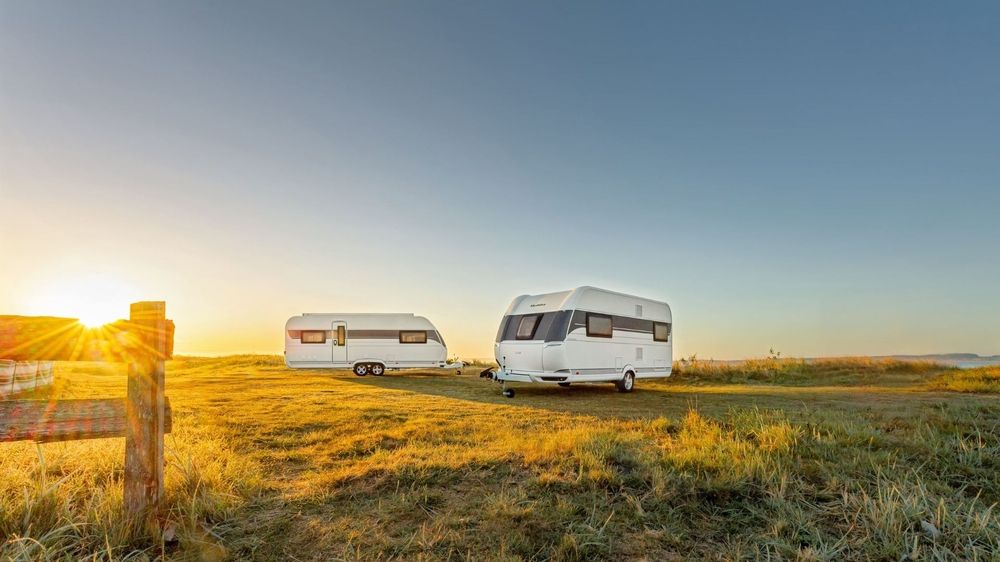 Zwei Wohnwagen stehen bei Sonnenaufgang auf einer Wiese mit Weidezaun
