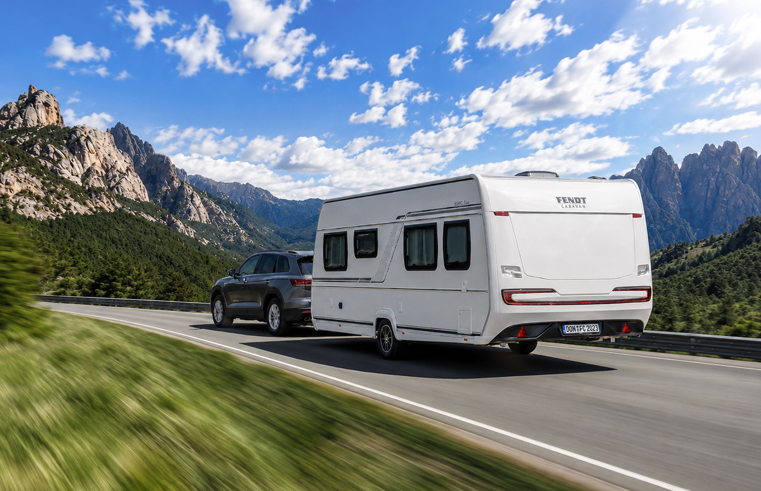 Weißer Fendt Caravan Wohnwagen wird von SUV auf einer Bergstraße in den Alpen gezogen