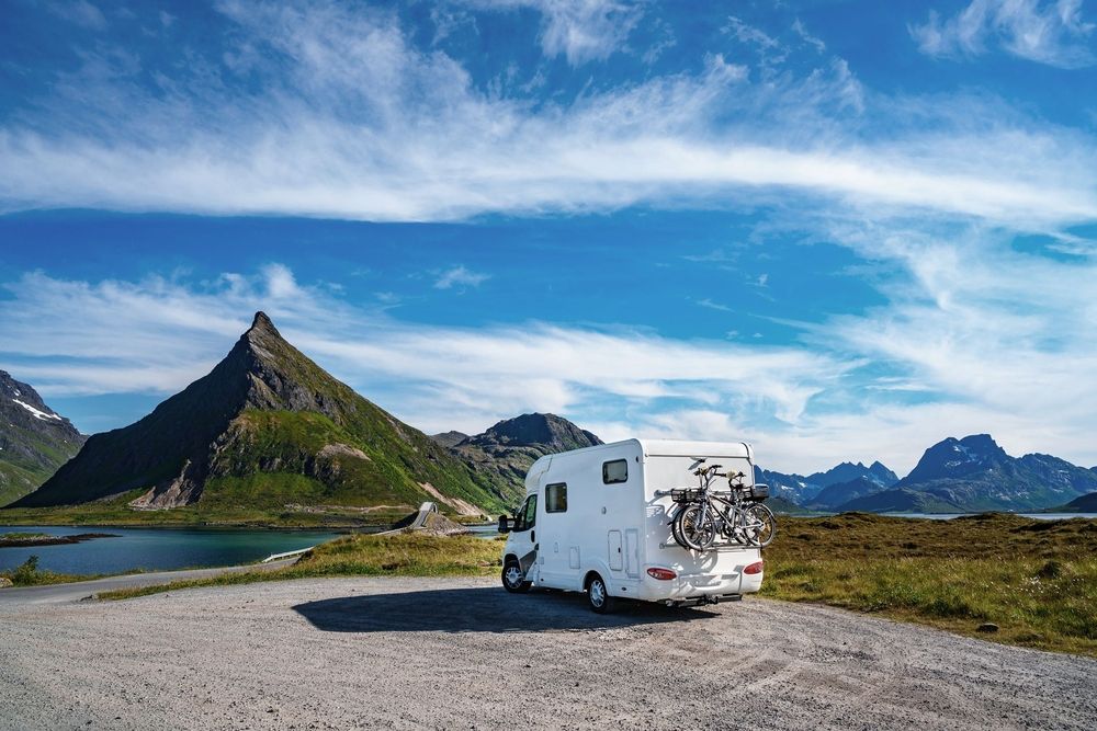 Weißes Wohnmobil mit Fahrradträger in Berglandschaft mit See und grünen Gipfeln